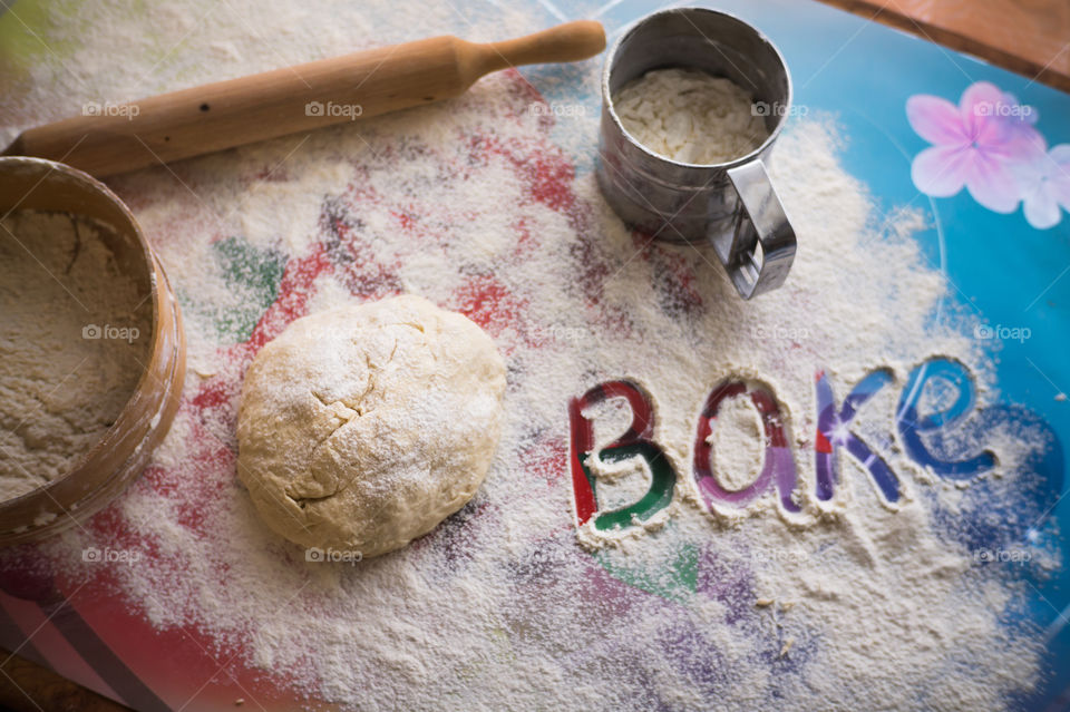 On the table lies a pastry for pies with sprinkled flour and a seeder for flour. Written to bake on the table.