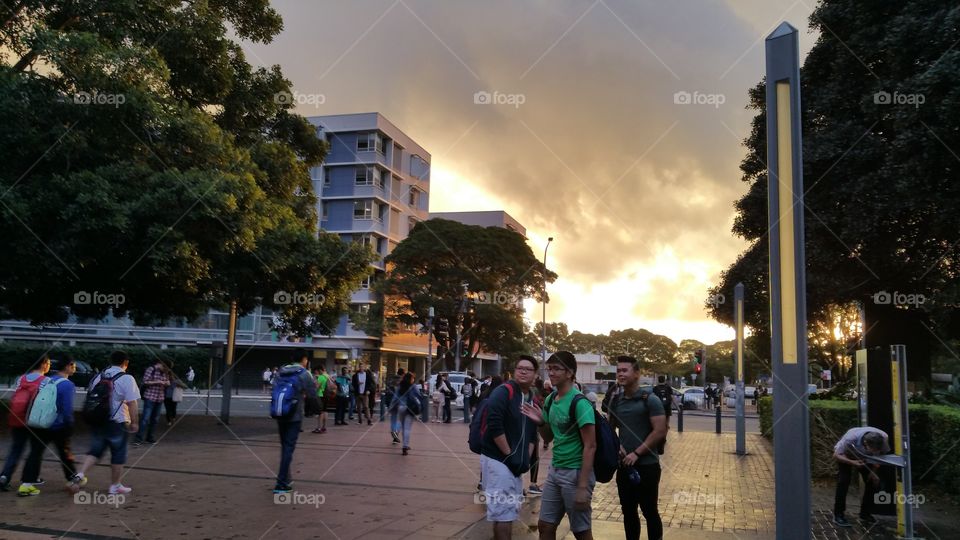 People around at the walk way late in the afternoon. The image is accentuated by the background colorful and dramatic clouds formation.