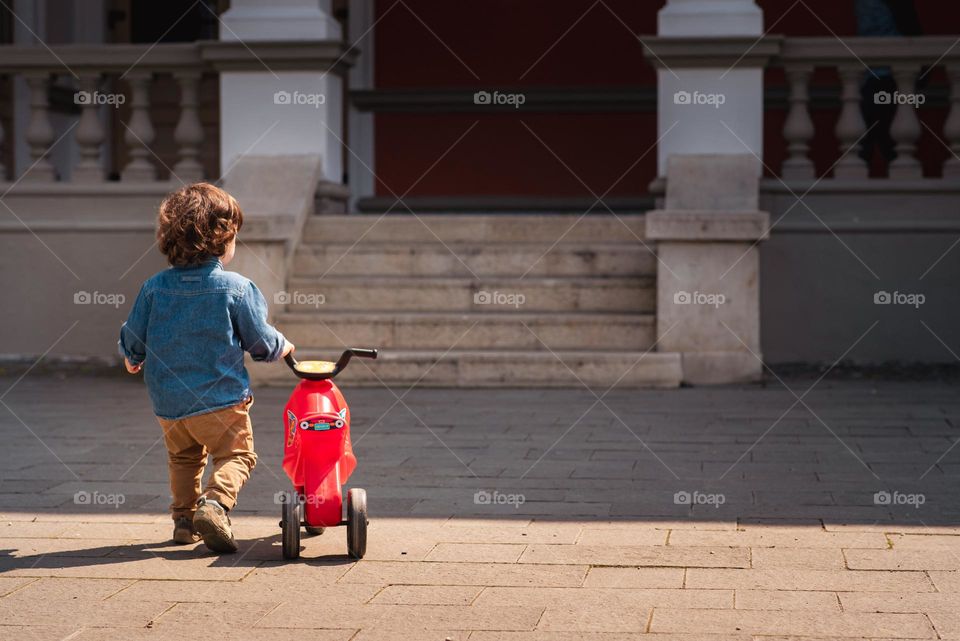 Toddler from the back holding his little red bicycle