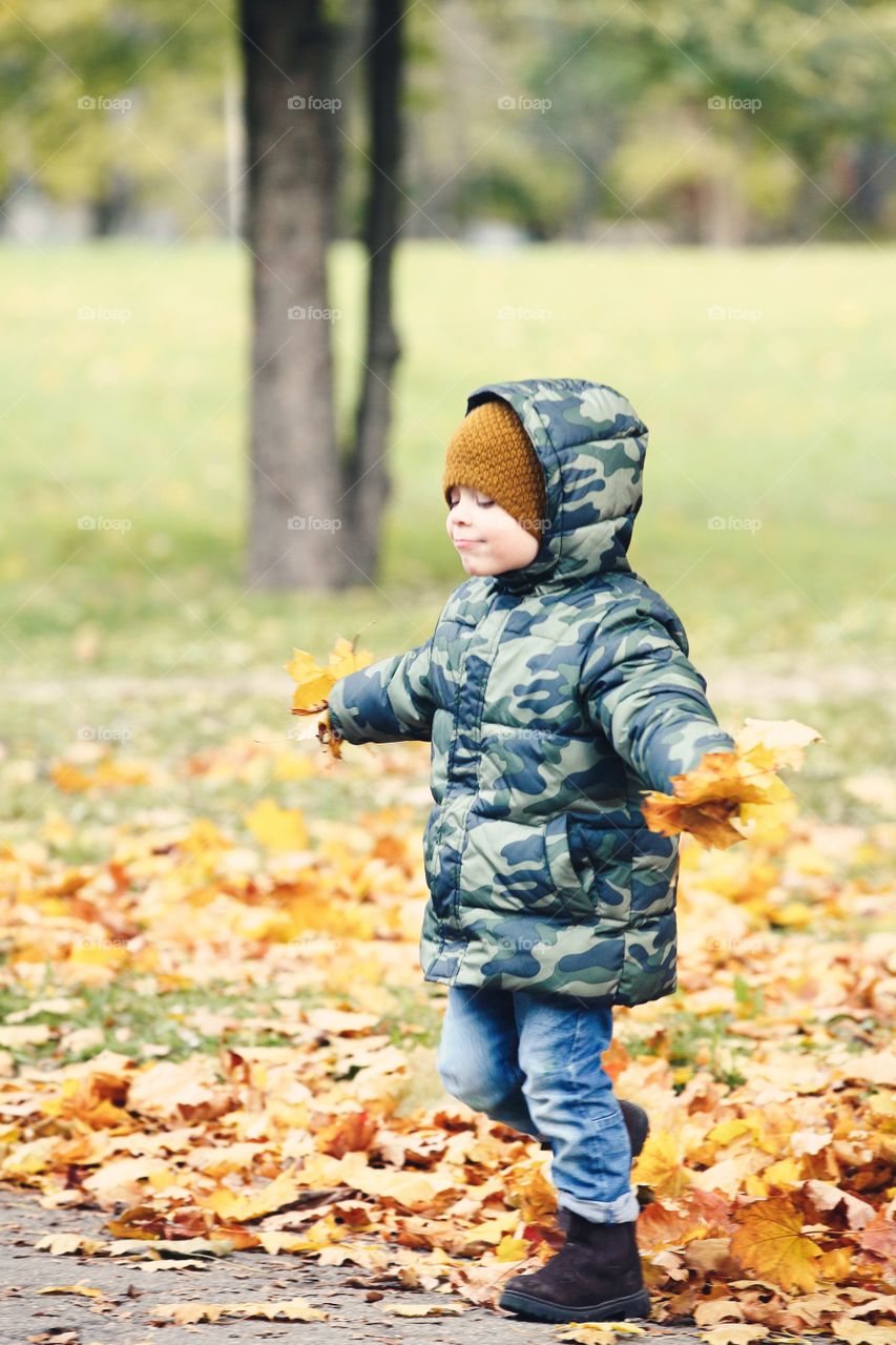 Little boy in the autumn park with yellow leaves in the hands