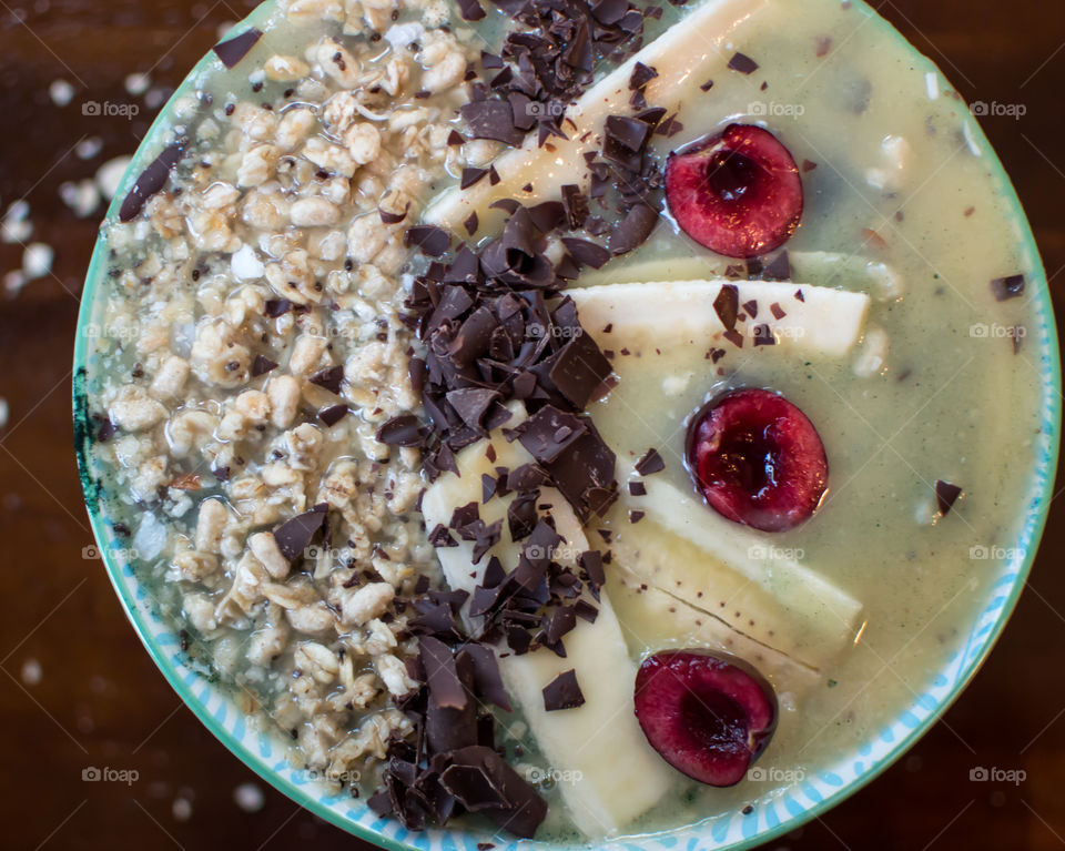 Antioxidant rich gourmet dark chocolate sprinkled on banana cherry oatmeal fresh fruit superfoods smoothie bowl with bee pollen and chia seed