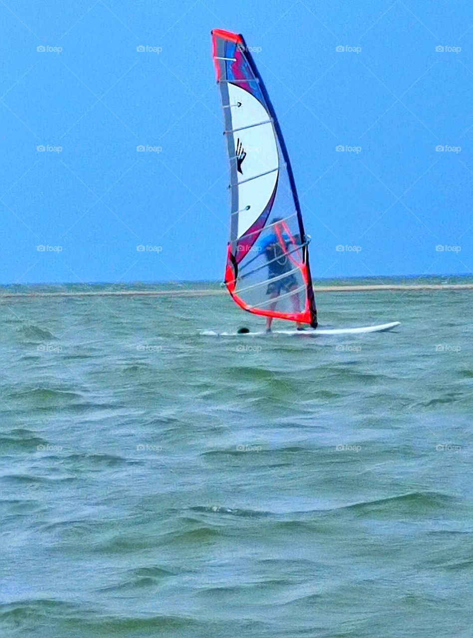 Summer.  Sea.  Windsurfing.  In the sea, on the waves, a man moves on a surfboard with a sail