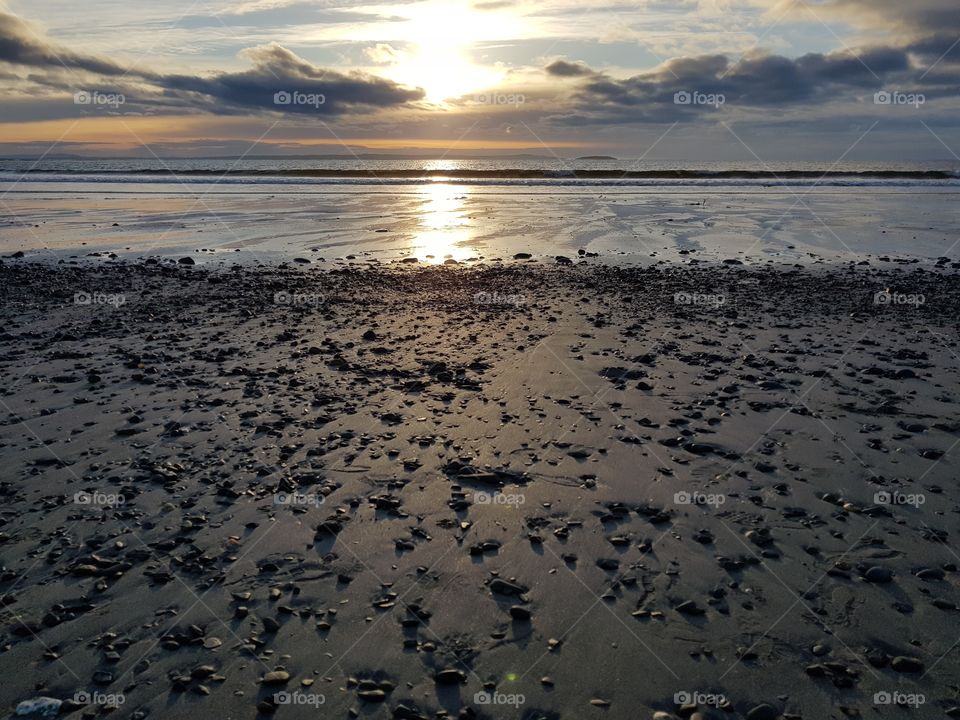 Sunset over a pebble strewn beach. Sun reflection on beach and water.