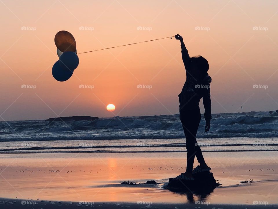 a young girl holding multicolour balloons against the sunset