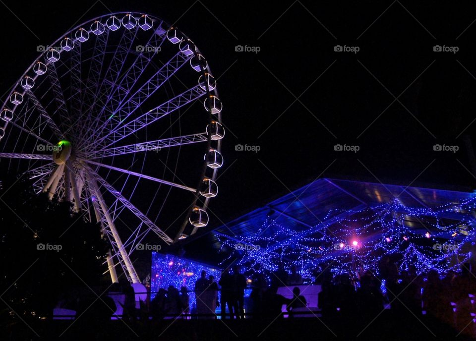 Night life scene, silhouettes illuminated by fairy lights. Ferris wheel