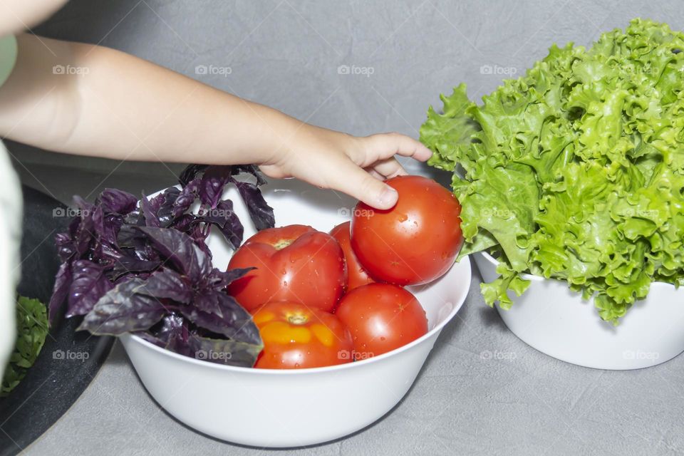 A small child helps to prepare a salad of fresh vegetables.