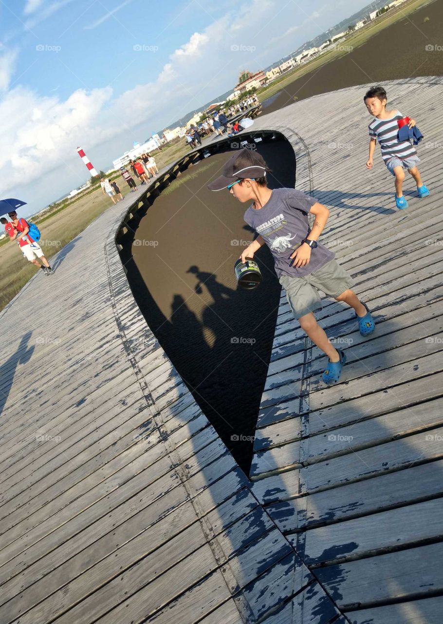 The art of composition: children playing at wooden path of seashore intertidal zone. very happy, delightful. because they want to see intertidal organism.