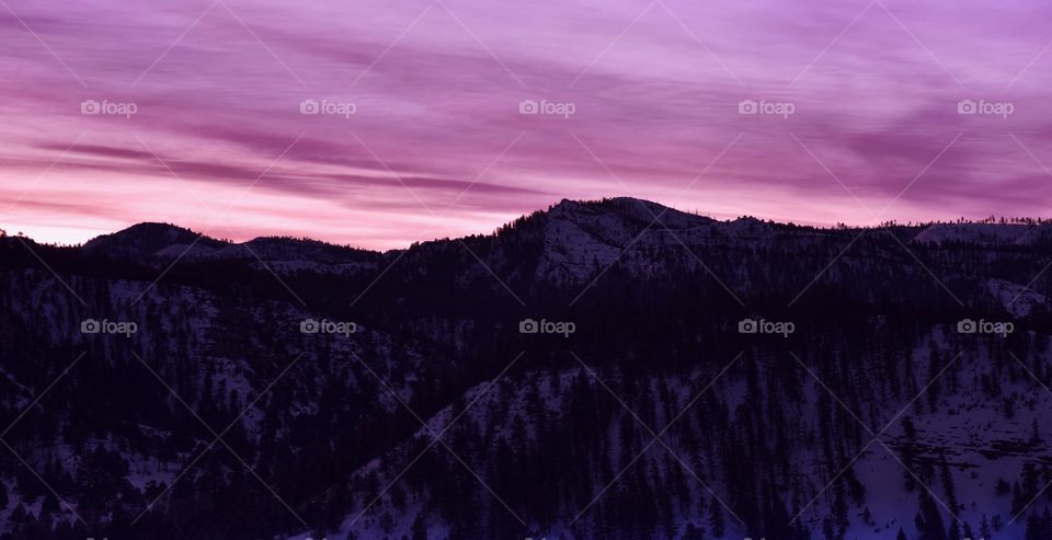 A pink and purple sky during sunrise. There is a snowy mountain in the foreground.