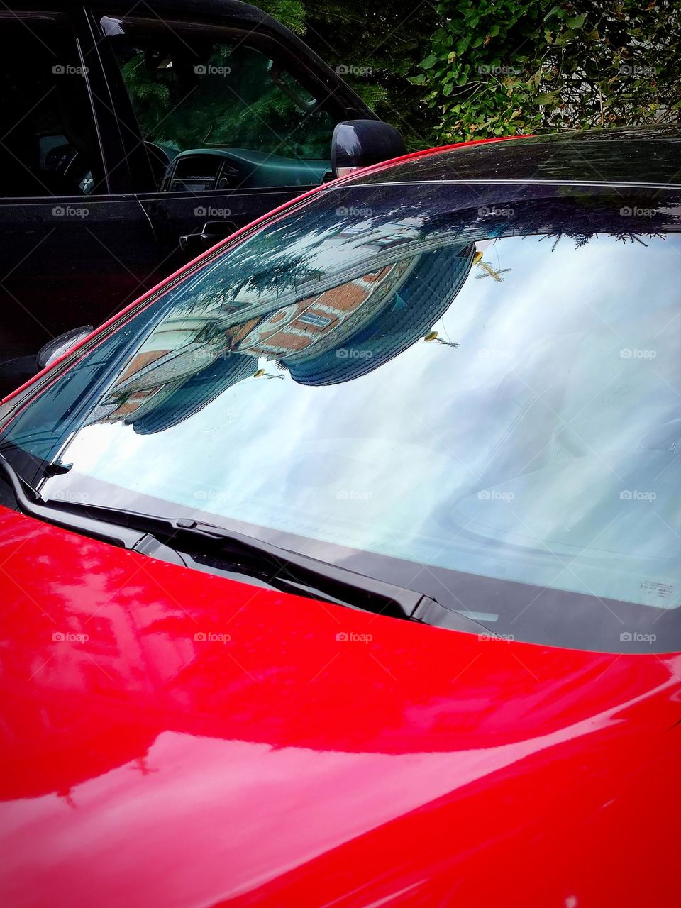 Cars.  The front of a red car, the windshield of which reflects the domes with crosses of an Orthodox church