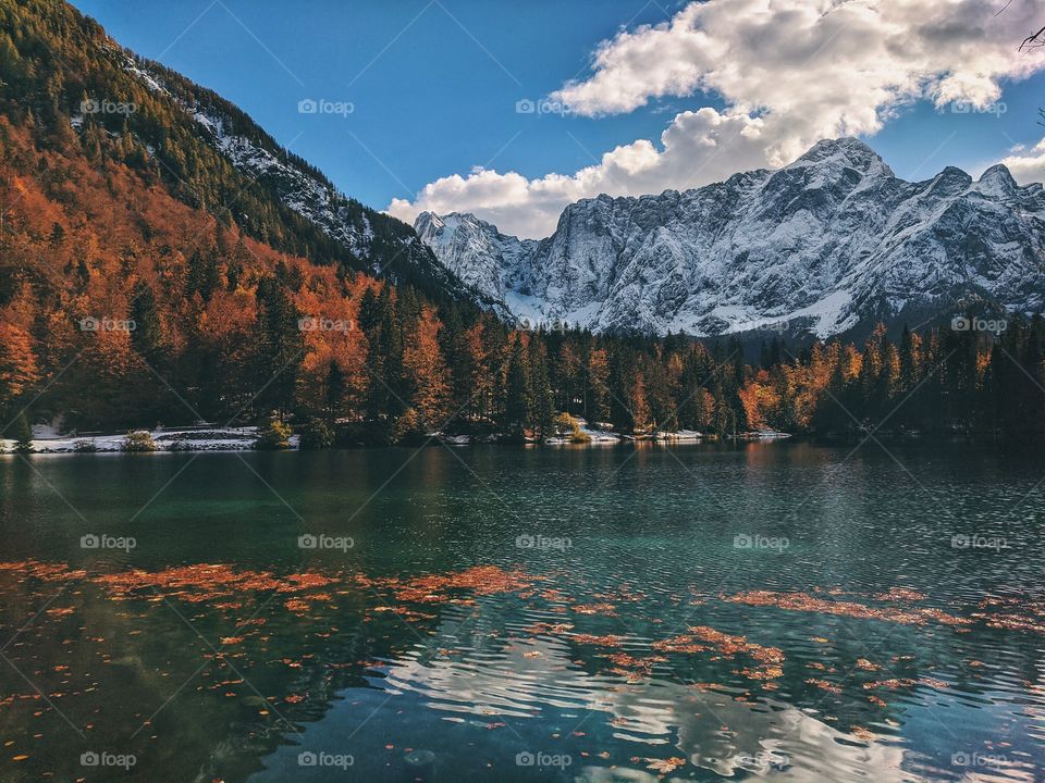 View of the autumn snow-capped mountain peaks against the backdrop of a transparent Italian lake.