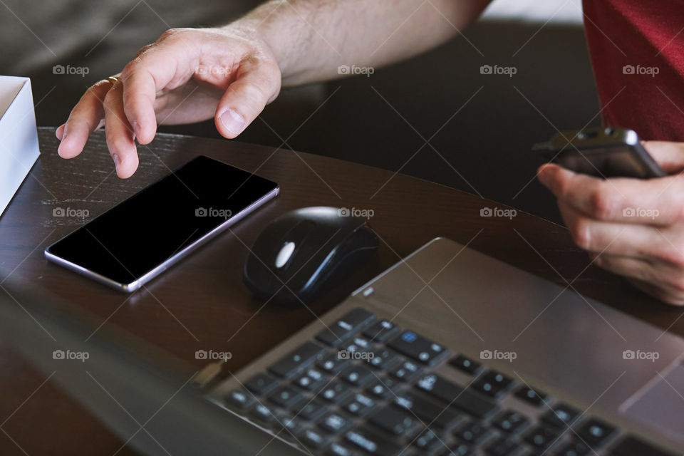 Man using smartphone working on laptop sitting at a desk