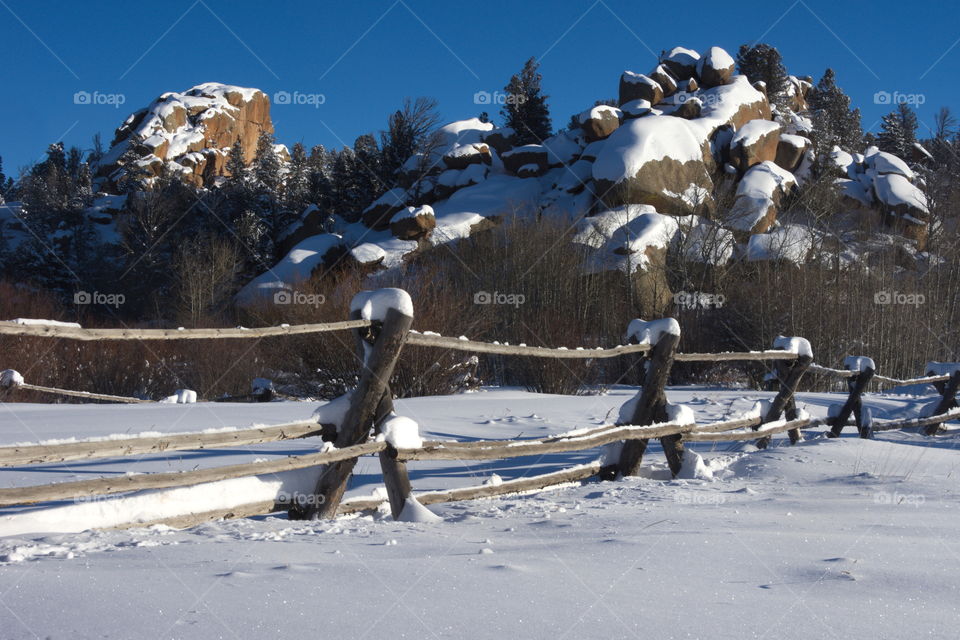 Large stone formations preside over a mountain valley.  A recent storm has covered the plain and the rocks in a fresh coat of soft snow, and a fence cuts across the foreground.