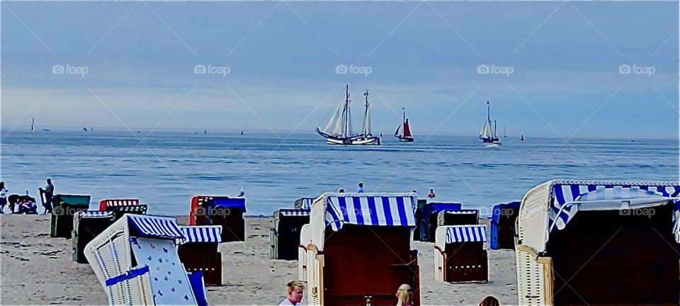 Like in a typical ocean resort movie scene the striped beach chairs await with their reclining comfort and fantastic views of large sailboats here at „Warnemünde“ by the „Ostsee“, the „Baltic Sea“ in former „East Germany“. 2023. Hypnotic Productions