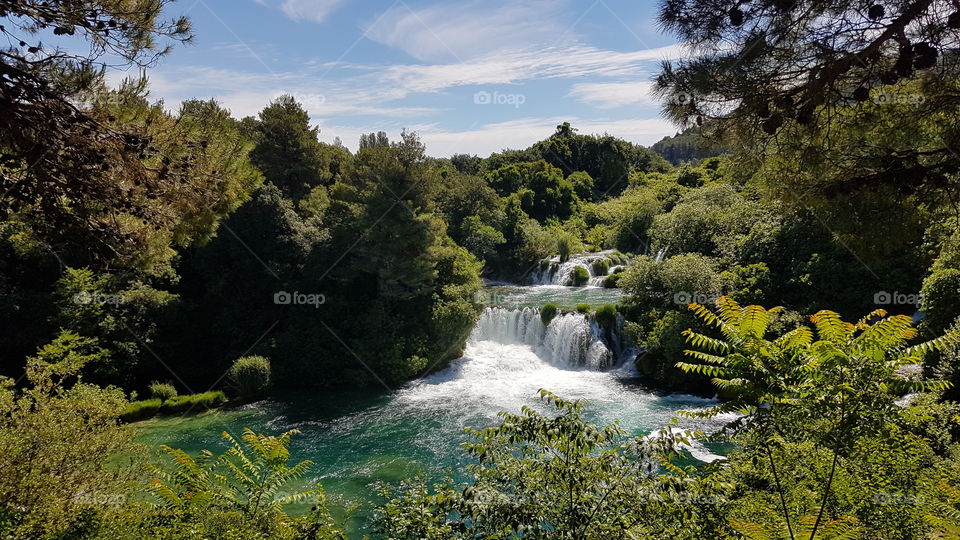 view of landscape, kirka waterfalls in Croatia, lush trees and plants around water on bright sunny day