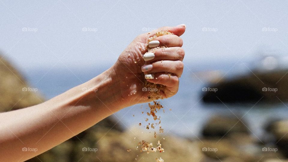 Woman manicure. Female hand pouring sand on the sea beach. Beautiful nails