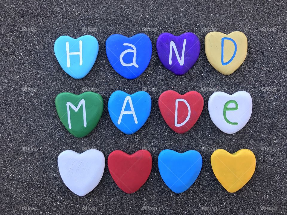 Handmade word with colored heart stones over black volcanic letters