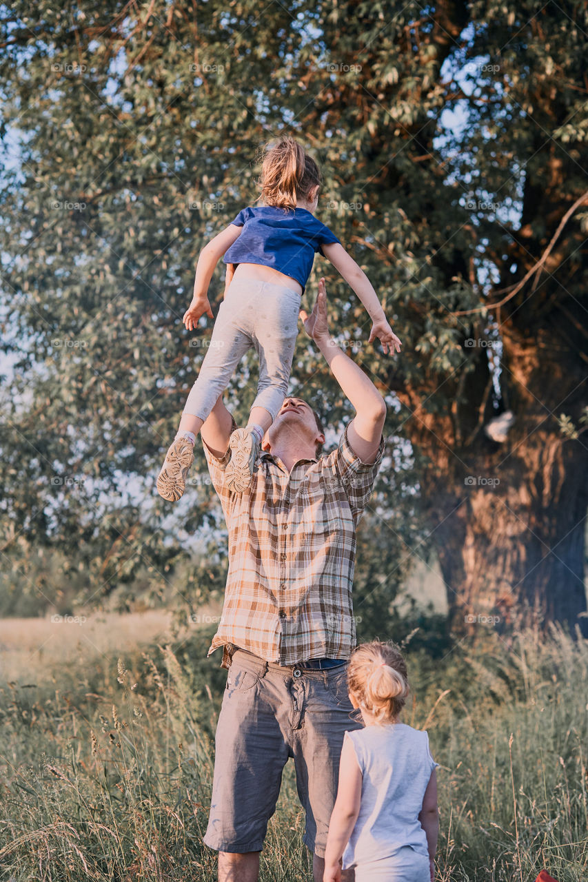 Father tossing little girl in the air. Family spending time together on a meadow, close to nature. Parents and children playing together. Candid people, real moments, authentic situations