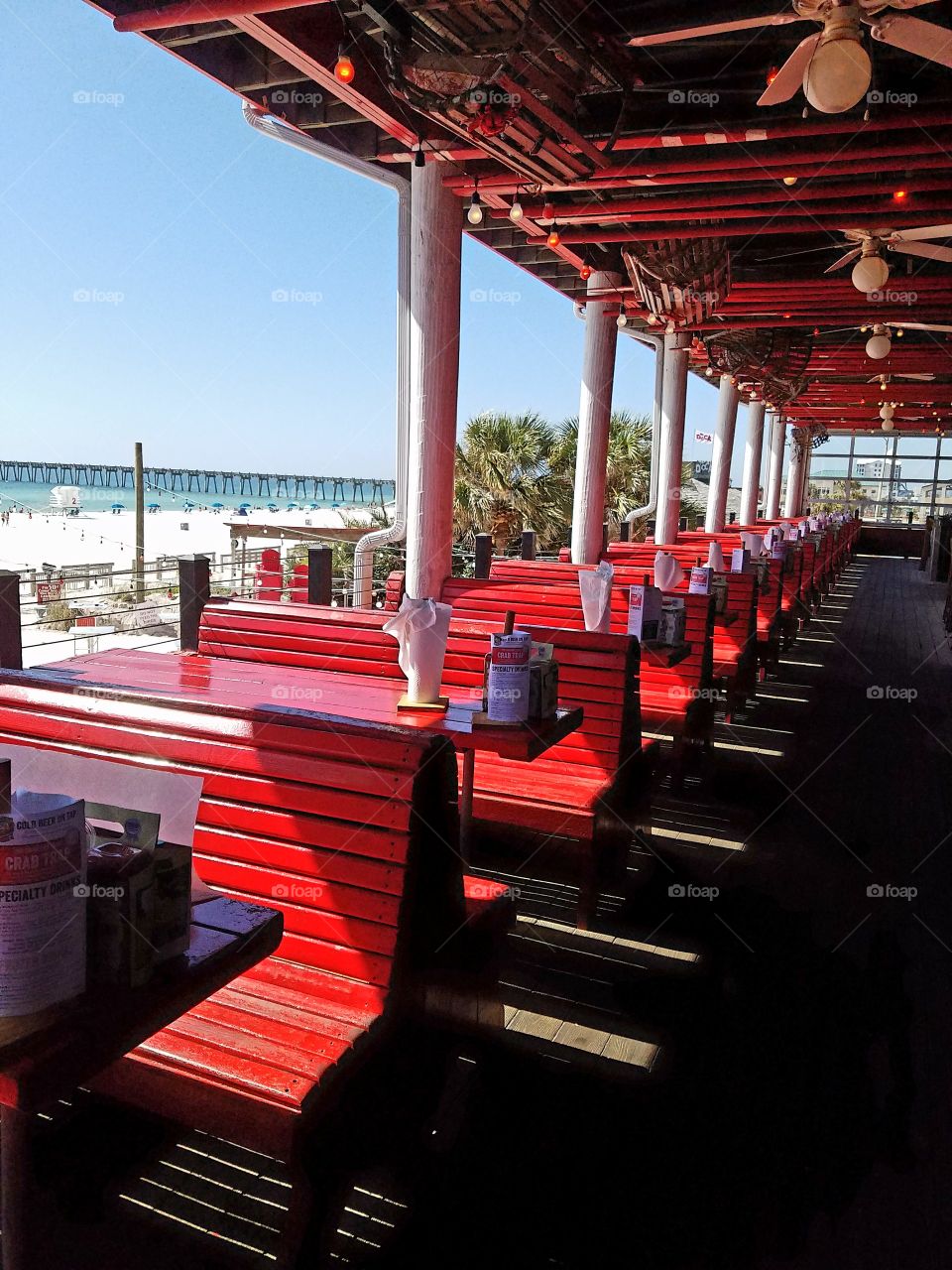Red tables and bench seats, white pillars, ceiling fans and natural wood floors.  Beach front restaurant on Pensacola Beach Florida.