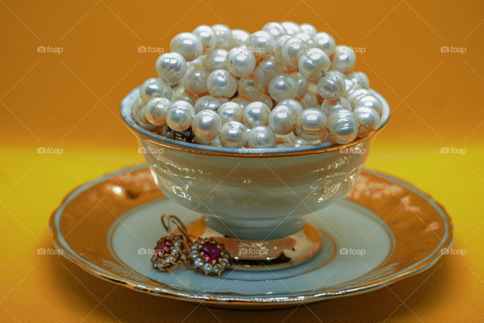 Tea cup with Pearl in it and earrings at the plate