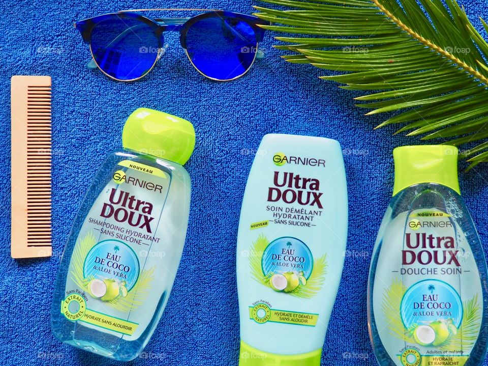 Garnier eau de coco shampoo, conditioner and bath gel on a blue towel with blue sunglasses and palm leaf.