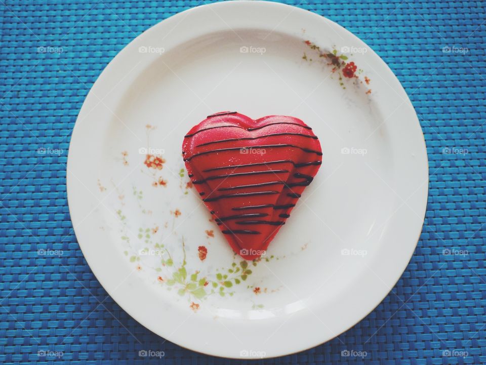 red heart-shaped cookie on a flower-painted flat wear on a blue background 