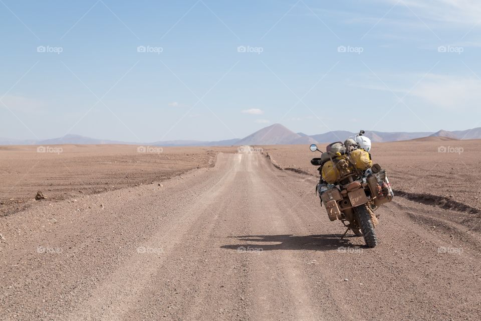 Desert view with motorcycle. Atacama desert road view with motorcycle parked on the right side. Dry gravel road leading towards hills. Adventure bike