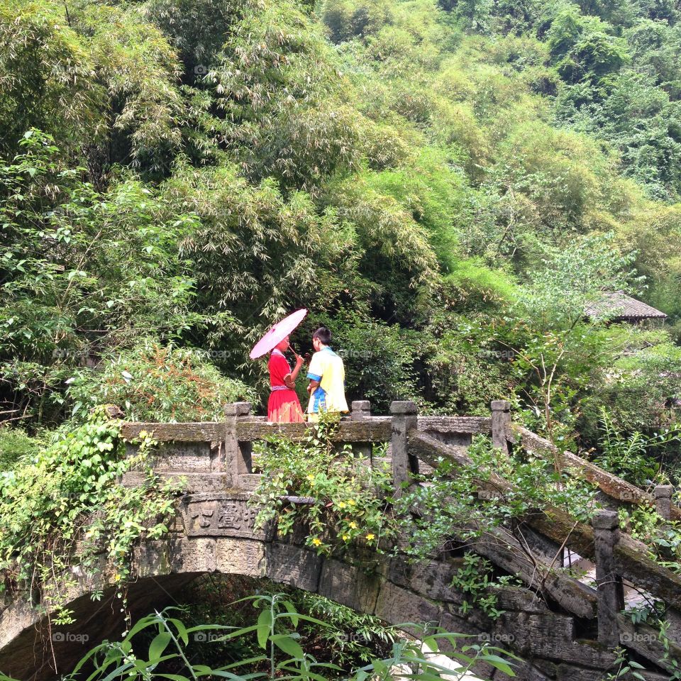 Traditional Dressed Chinese Young Couple. Young Chinese Couple Standing On Bridge Wearing Traditional Chinese Costumes In Forest Area