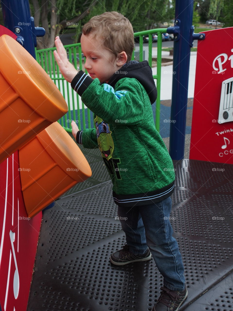 A little boy enthusiastically plays on the plastic drums on a play structure in the park. 