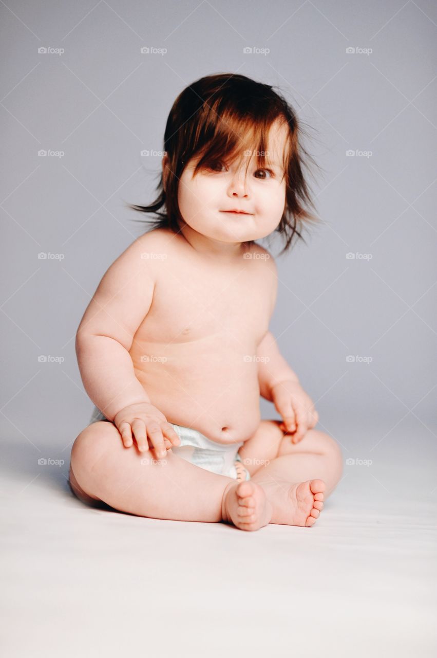 Baby girl sitting in diaper against gray background