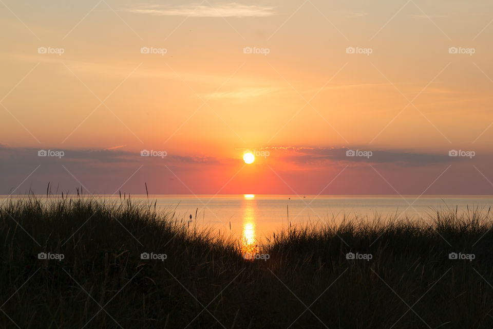 Beautiful orange colored sunset by the ocean, sun reflection on calm peaceful water 