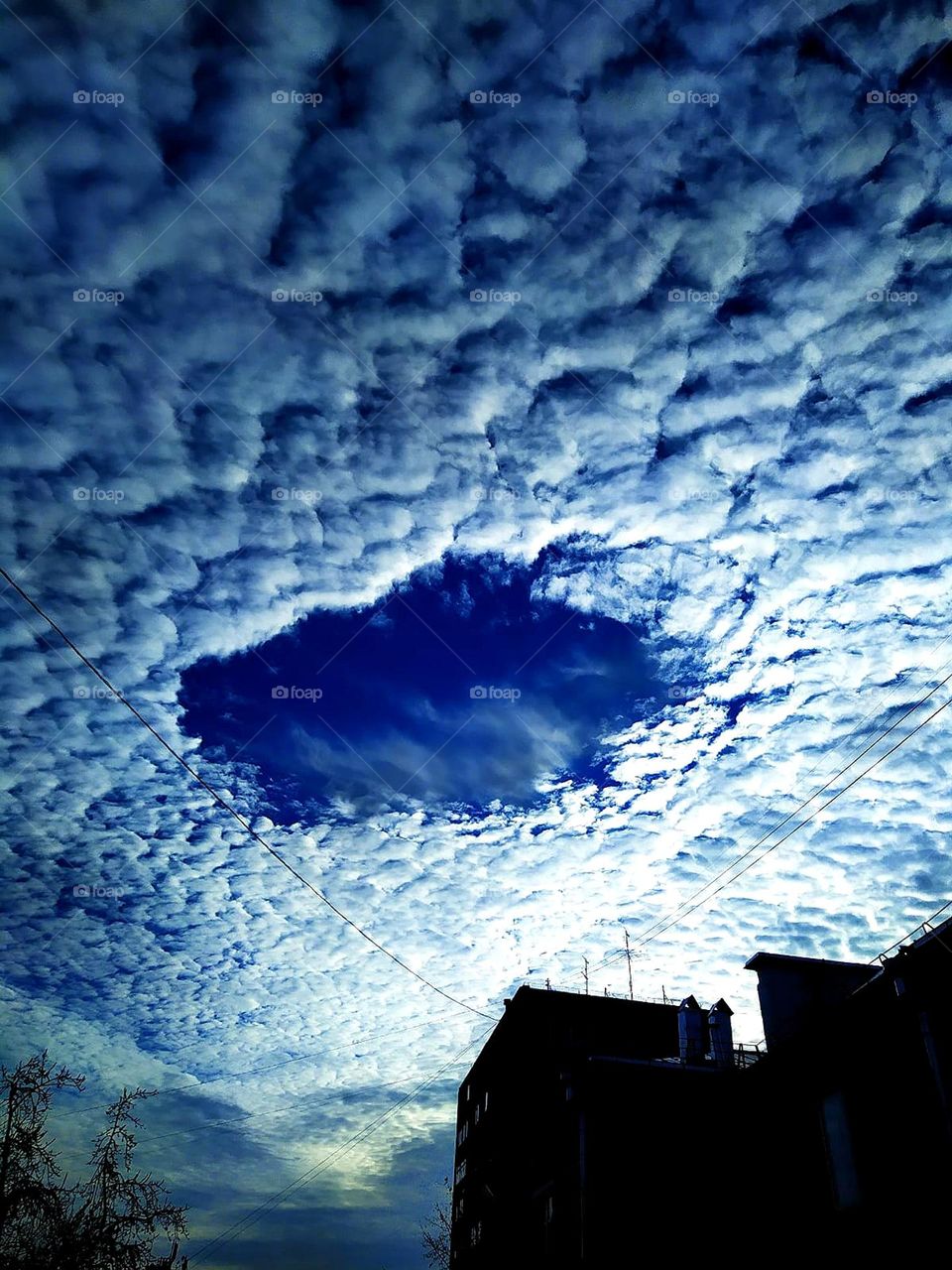 Clouds.  Dawn.  Dark clouds over the houses.  A round hole from the clouds in the center and you can see the blue sky.  Cloud donut