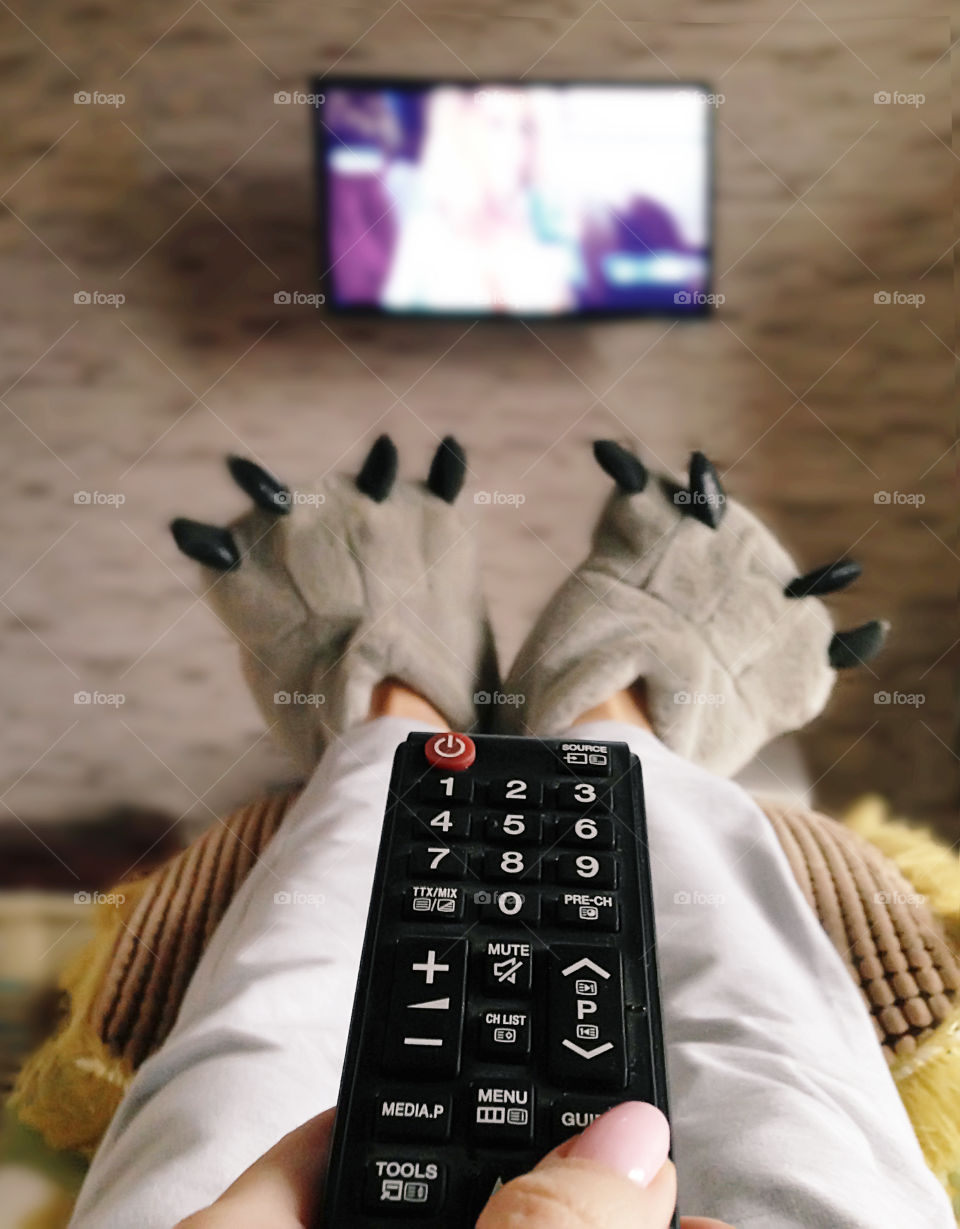 Watching television in funny cozy slippers at home 