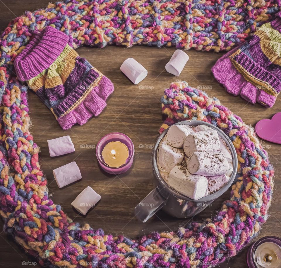 Hot chocolate and marshmallows surrounded by colourful winter woolly scarf and gloves