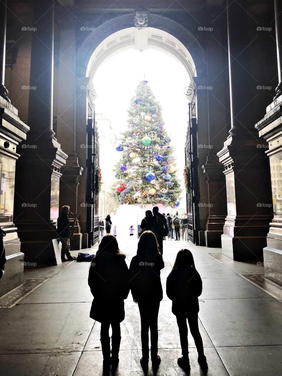 Children in silhouette looking up at Christmas tree in a city. 