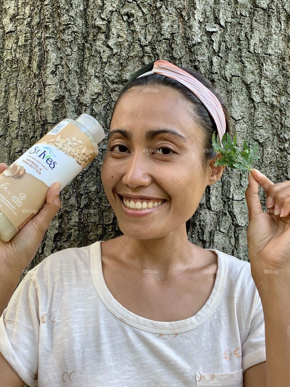 Energetic smiling person holding St. Ives oatmeal shea butter soothing body wash against a big tree. 