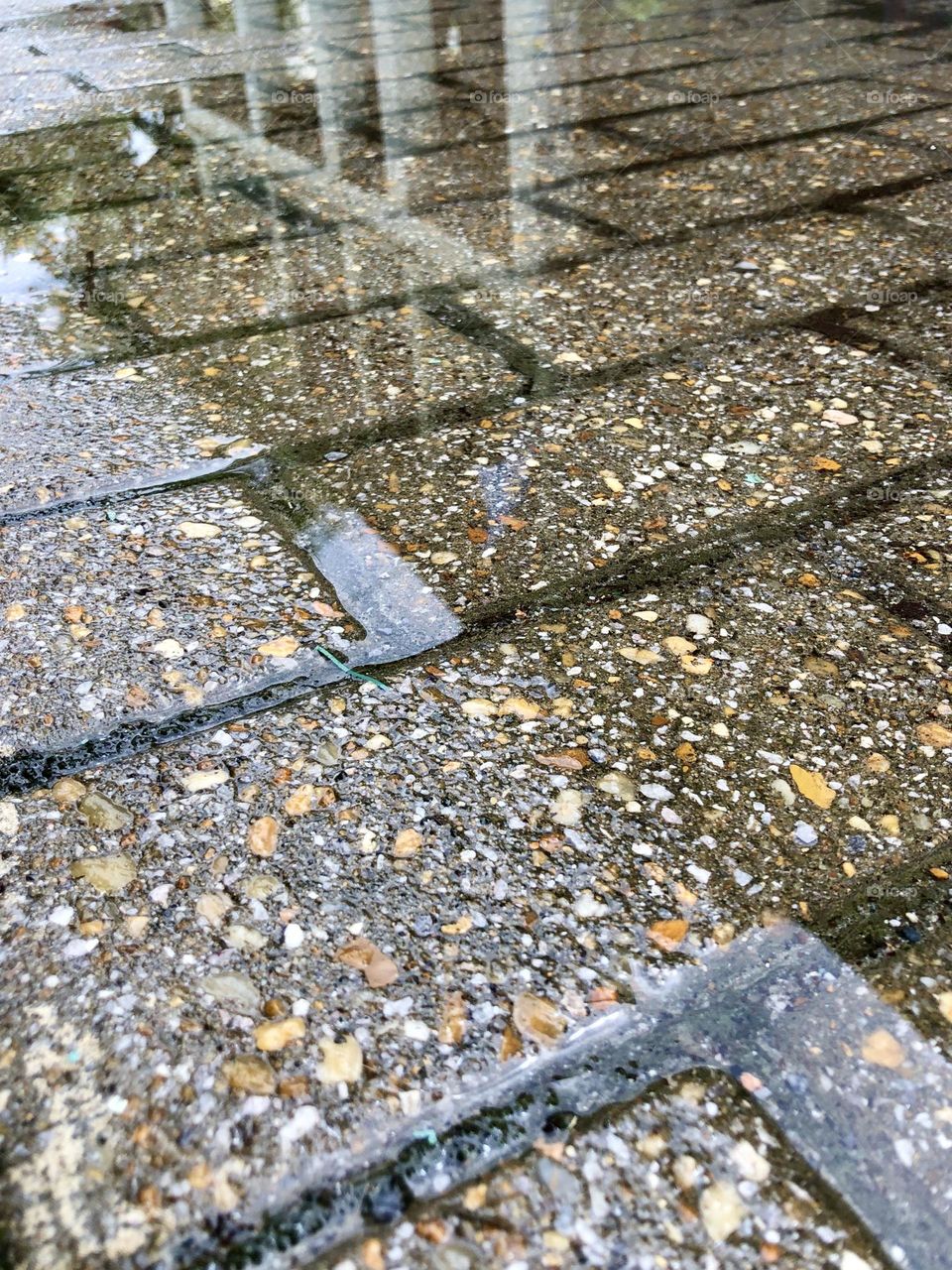 Low angle closeup of city brick sidewalk. The rain has covered the stones and offered a partial reflection of the urban scene