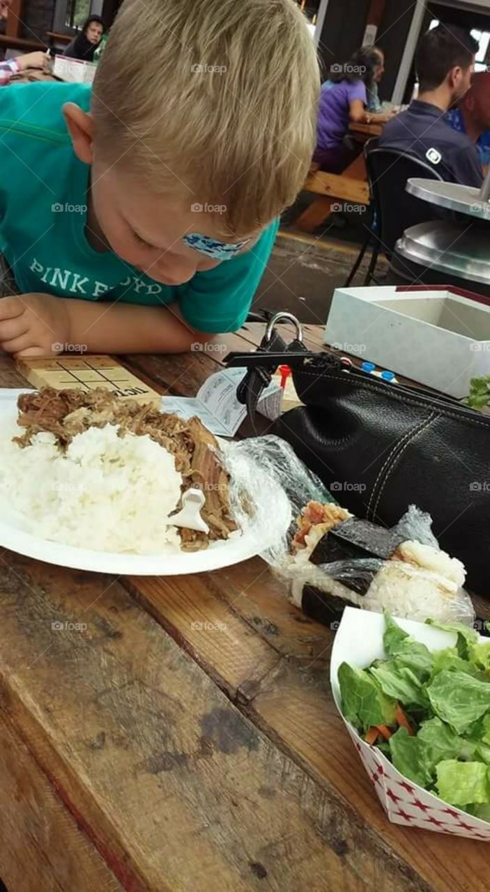 Little boy with bandaged head, looks in awe at his Hawaiian lunch plate.