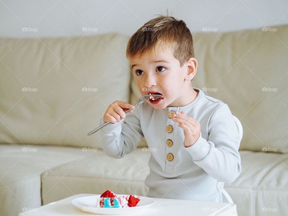 Pretty Caucasian toddler boy in grey pajama eating a cake 