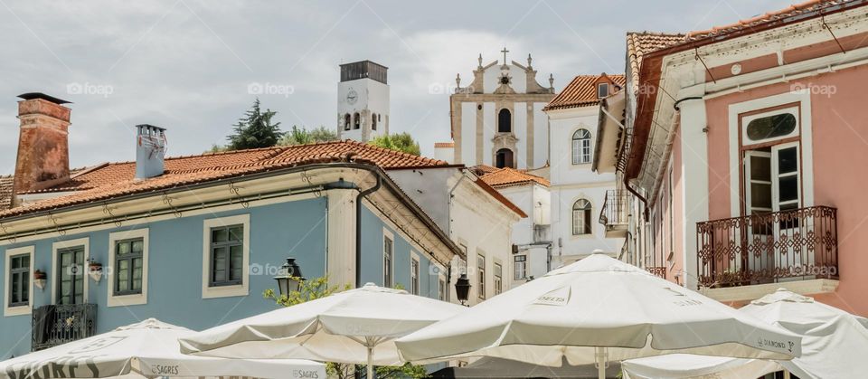 The town of Miranda do Corvo, with cafe umbrellas, painted buildings leading up to a clock town and Igreja Matriz de Miranda do Corvo.