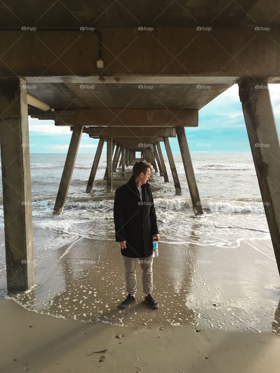 Young man in black coat on beach below jetty south Australia Glenelg Adelaide 