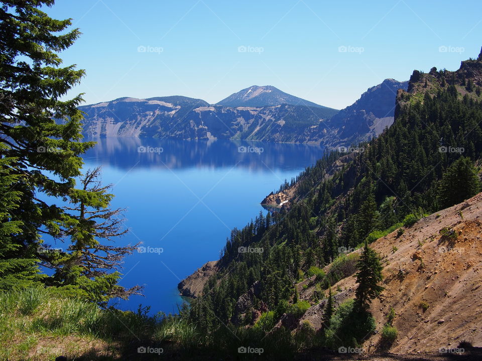 The jagged rim reflecting into the rich blue waters of Crater Lake in Southern Oregon on a beautiful summer morning with perfect clear blue skies.