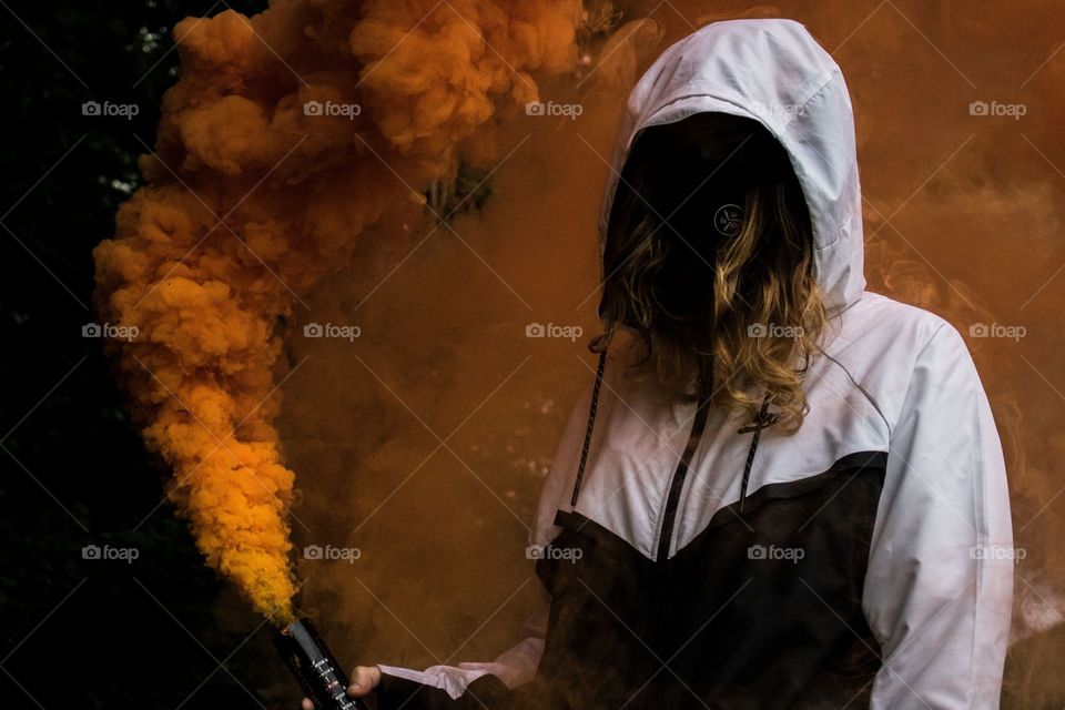 a hoodie wear, holding colourful smoke grenade