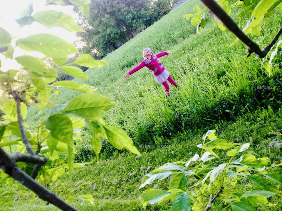 Gorgeous cloudy afternoon and little girl in bright pink colors is thoroughly enjoying it surrounded by a beautiful green grassy field and trees! 