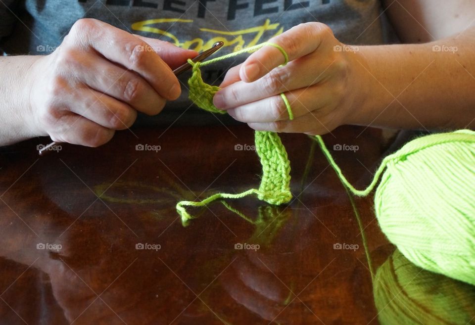 Bright green yarn ball and woman's hands are reflected in the table top