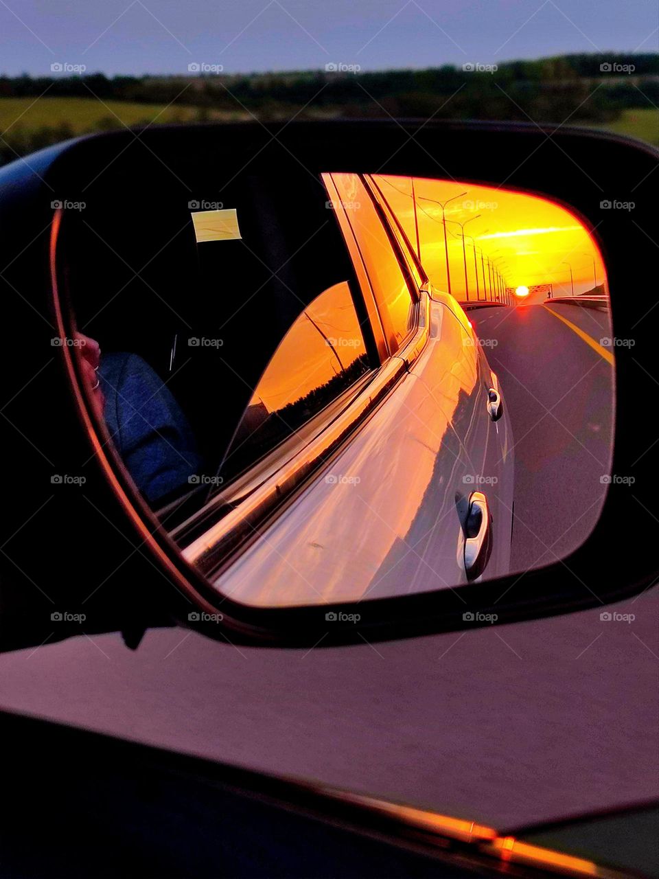 Travel by car. The road is reflected in the side mirror of the car, the sunset is on the horizon. The ability to get to any place: mountains, fields, sea. Anticipation of new adventures