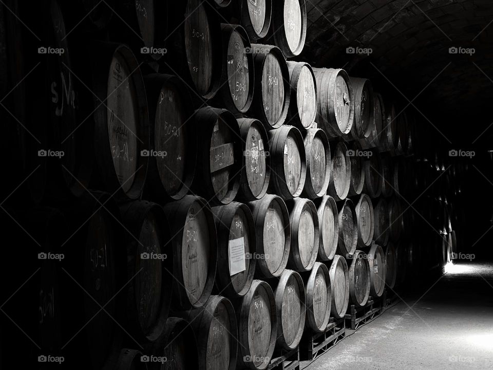 Group of brown barrels stacked in a dark corridor illuminated forming a curious pattern, taken in monochrome style.
