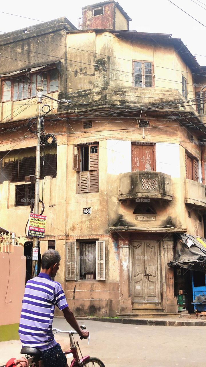 This is a street photograph of an old building. One man is cycling in front of the building. This place is 18/24 Ballygunge Fern Road in Kolkata.