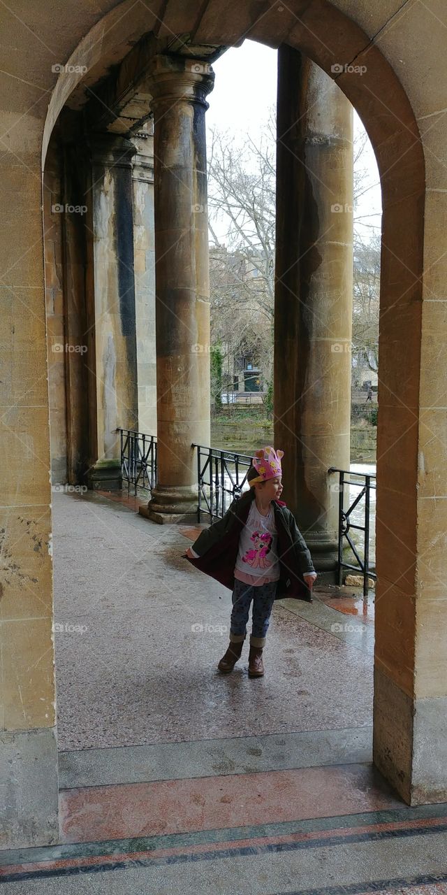 little girl twirling in arches of building in winter