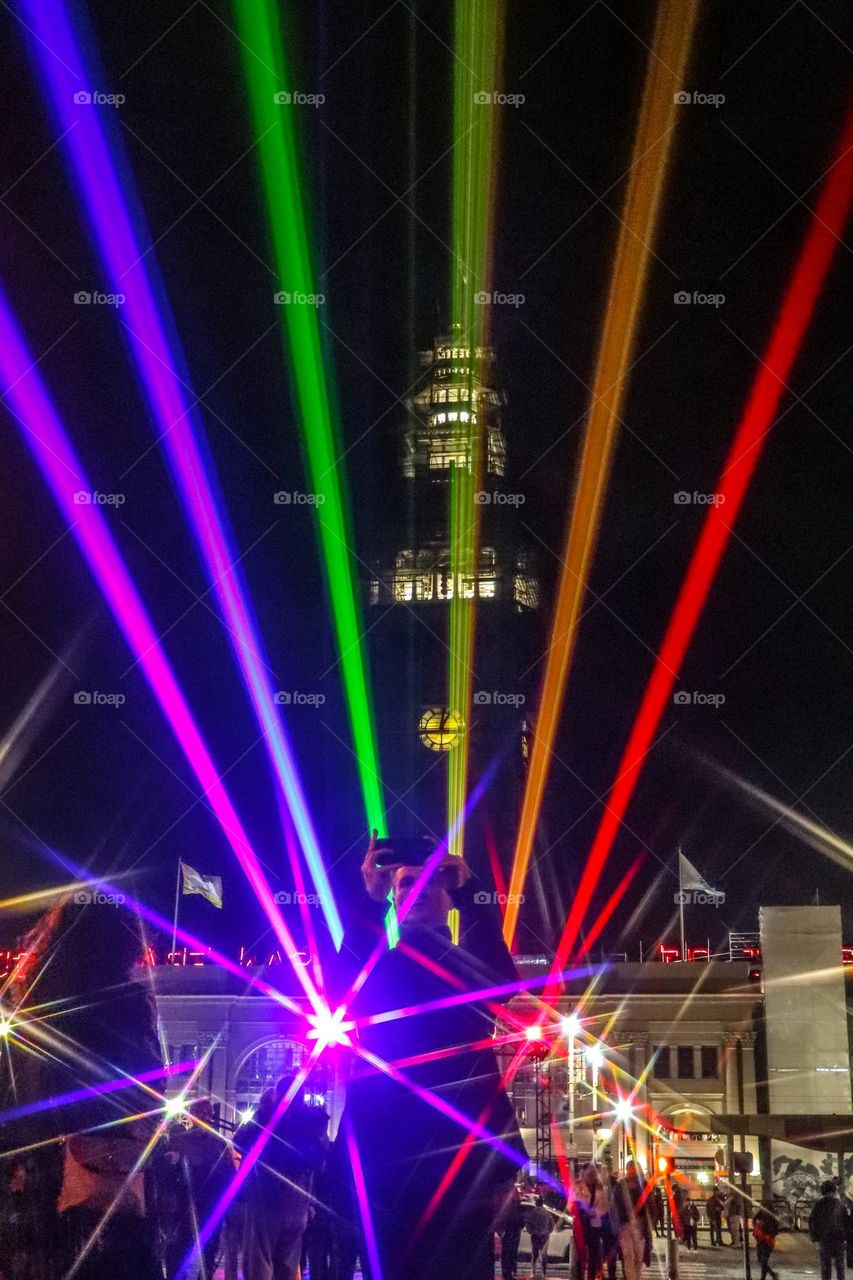 San Francisco Pride 2023 laser light display of the pride flag colors illuminating the sky in front of the Ferry Building on the Embarcadero as people gather to celebrate 