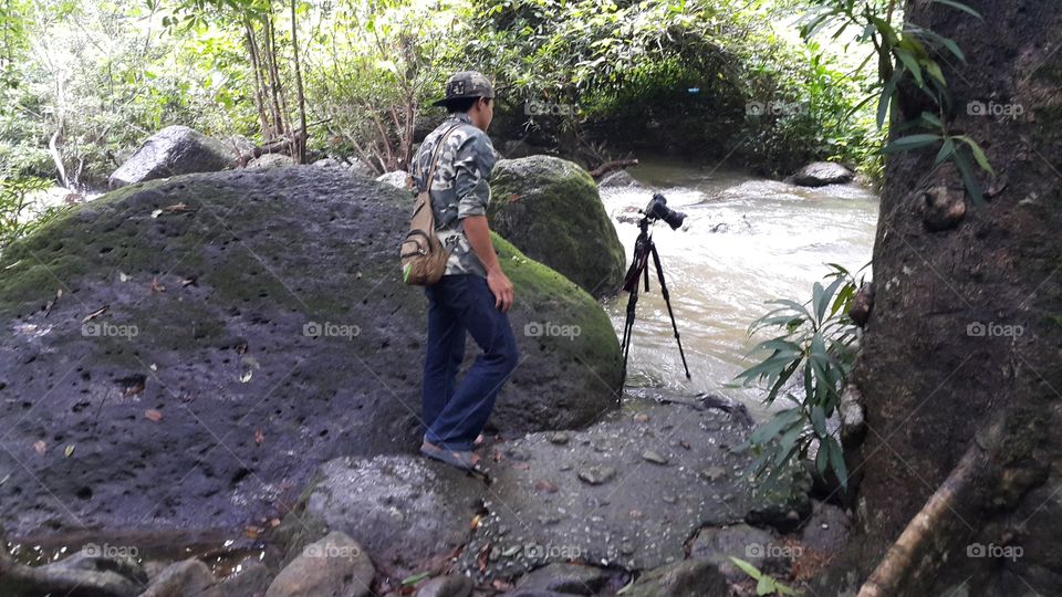 photographer set up camera on a tripod for a long exposure shot of a river in rainforest Thailand